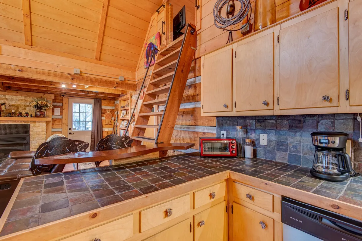 This image shows a kitchen with a countertop featuring slate tiles, visible appliances, a decorative wooden ladder, and a fireplace in the background. Wall art and warm lighting enhance the cozy, lived-in feel, while the tile details echo the section’s emphasis on style.