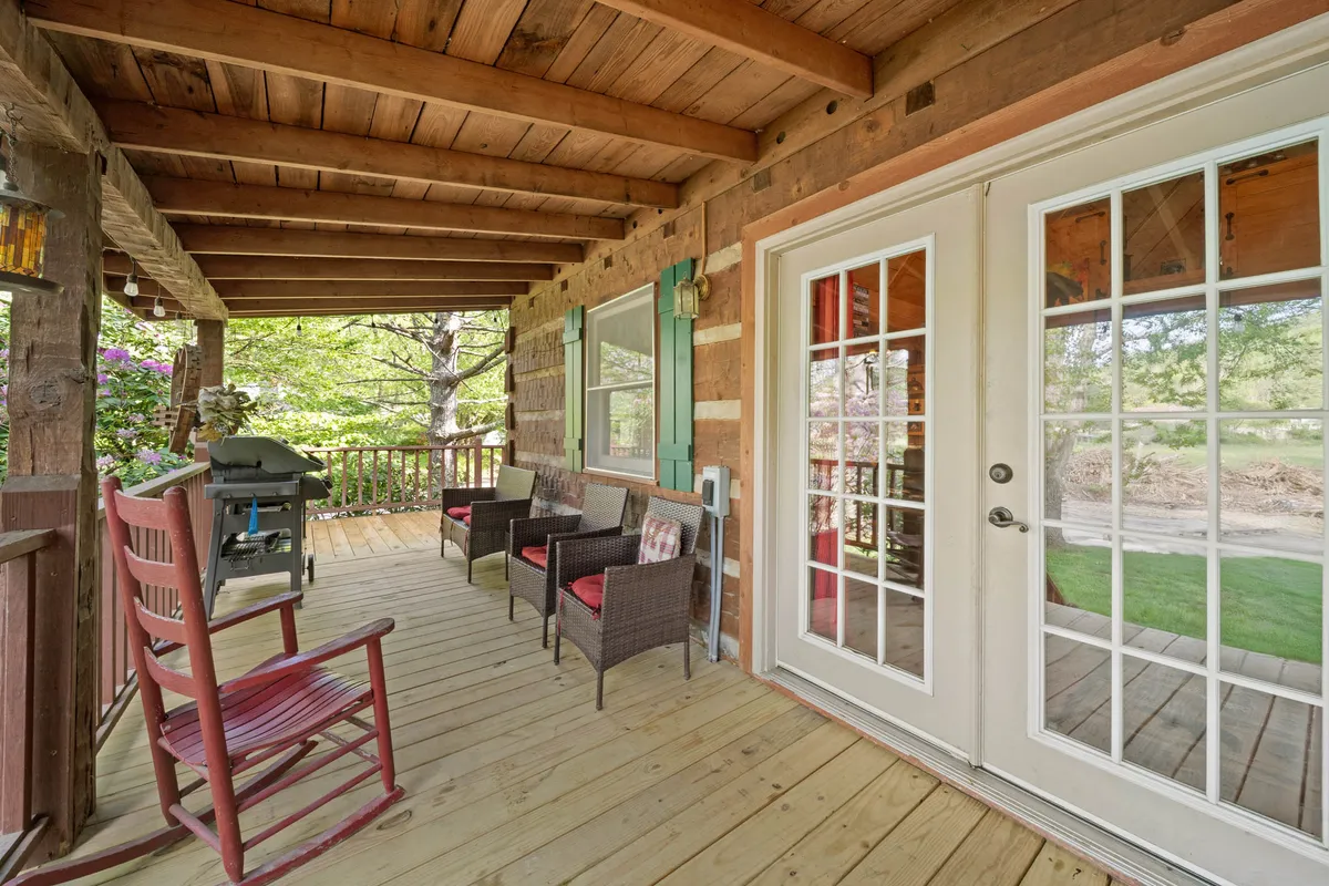 This image captures a relaxed outdoor living space with a rocking chair, wicker seating, a grill, and double doors opening to the greenery beyond. The inviting setup is perfect for morning coffee, evening barbecues, or social gatherings after a day outdoors.