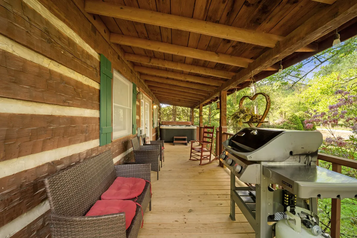 A covered porch with cushioned rocking chairs and a grill, perfect for enjoying the outdoors while staying close to the comfort of the cabin. The space is set up for relaxation, socializing, and morning coffee with views of the river just beyond.