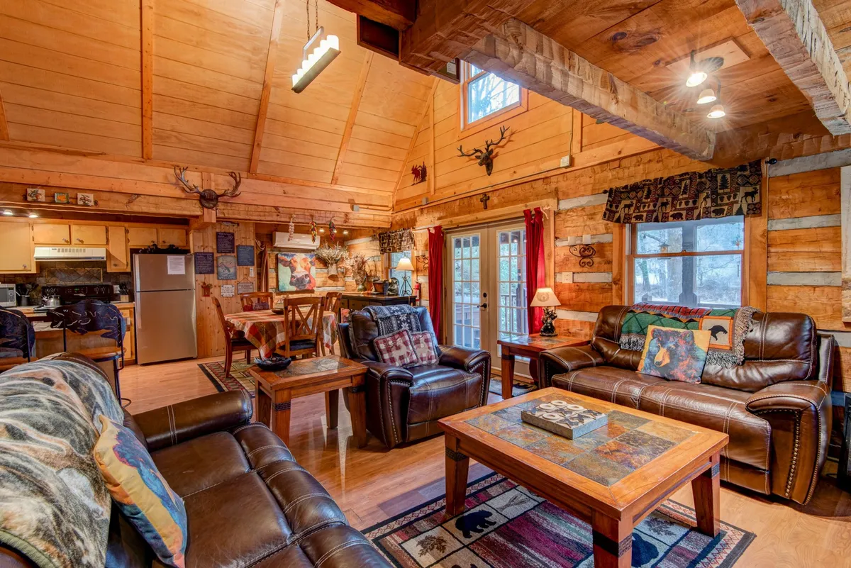 A spacious room with leather sofas facing a wooden dining table, illuminated by large windows that showcase natural light. Decorative wall art and the open layout foster a sense of gathering, seasonal celebration, and connection to the outdoors.