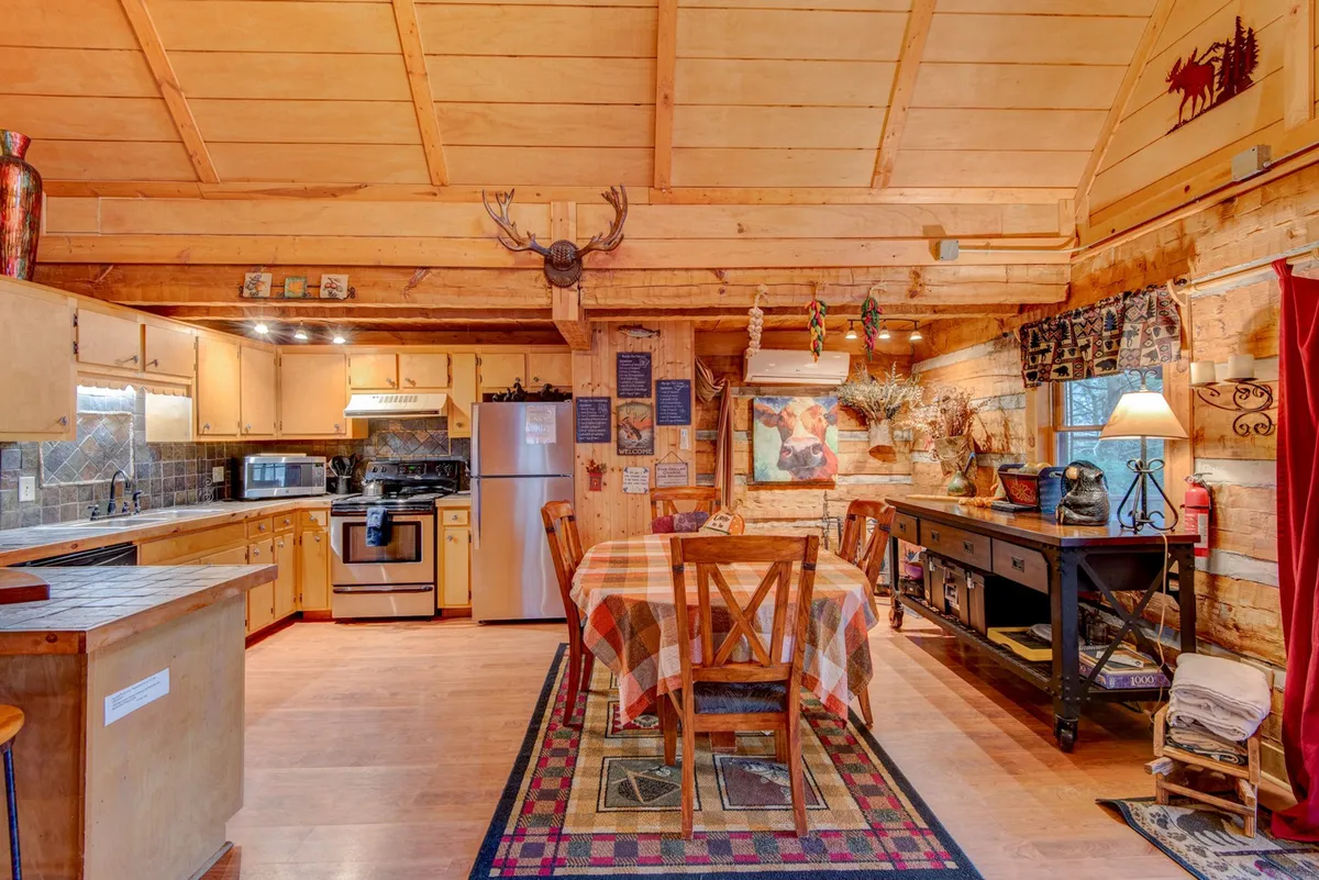 The photo showcases a cozy dining area with a dining table placed adjacent to the kitchen counter, decorative elements like a moose head, and a window with curtains that allows plenty of natural light. This setup is perfect for family meals and encourages togetherness.